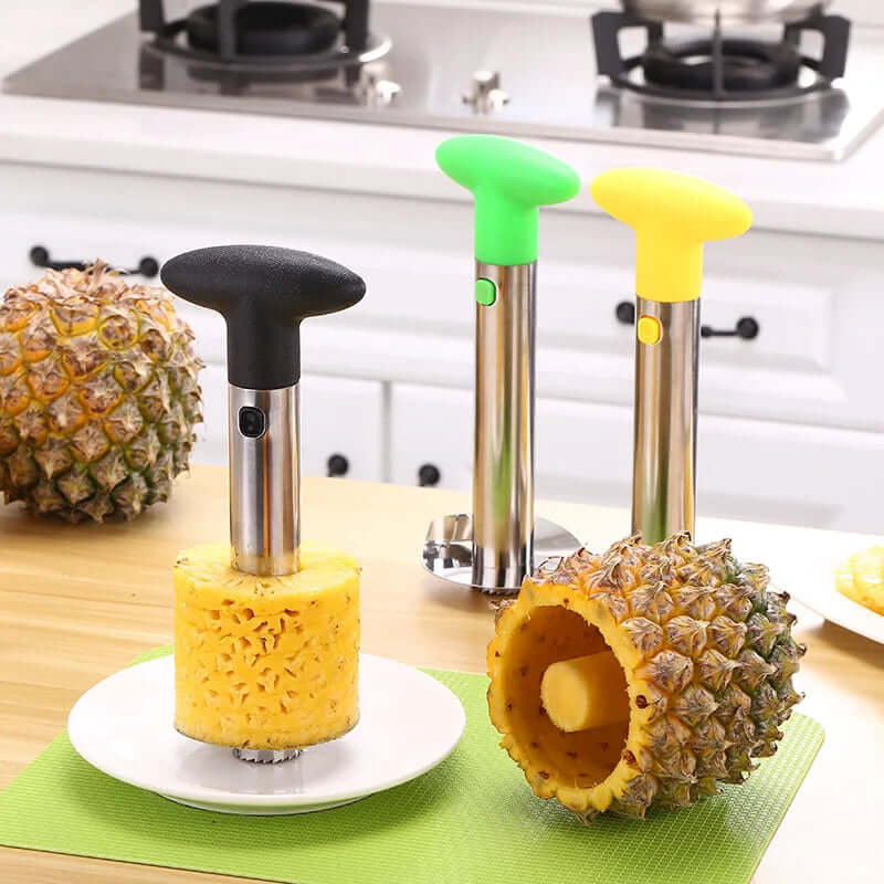 Stainless steel pineapple corer and slicers with green, yellow, and black handles on a kitchen countertop.