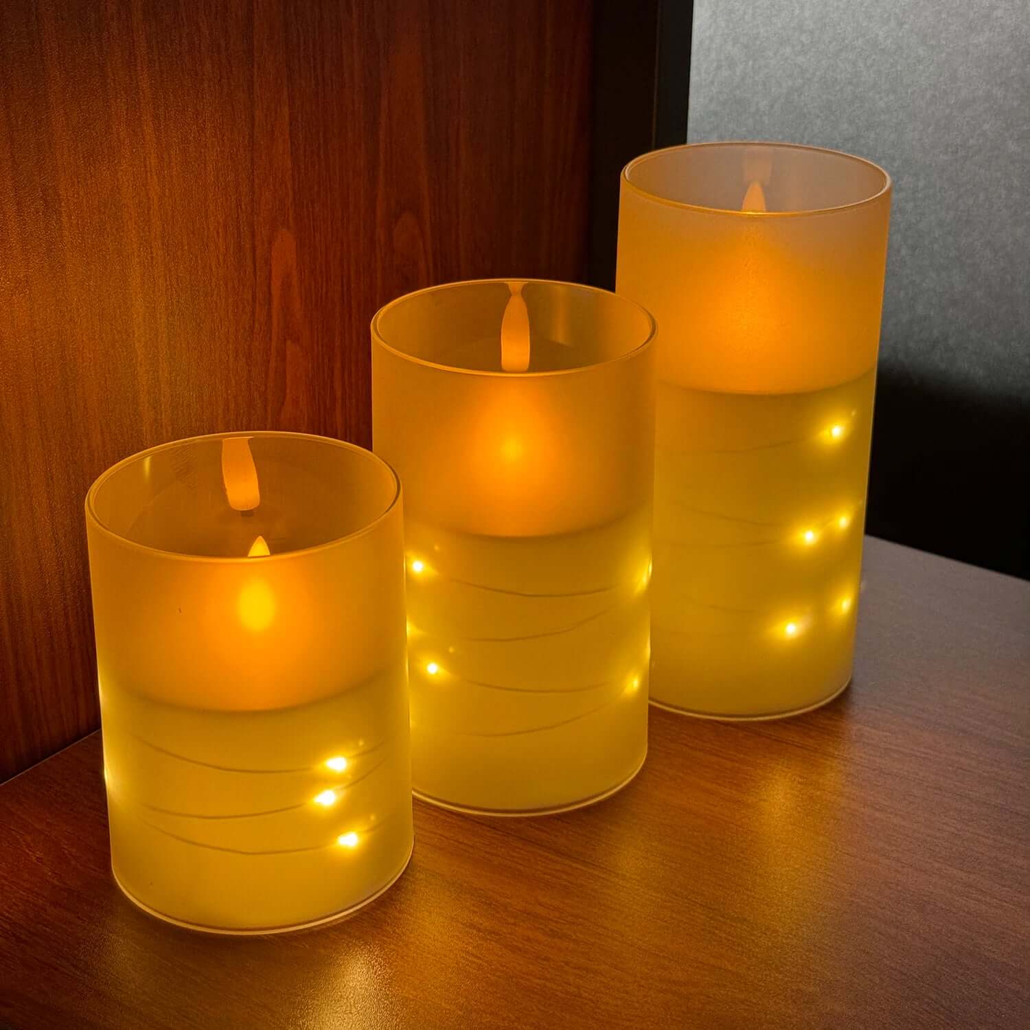 Set of three warm yellow LED electronic candles glowing softly on a wooden surface.