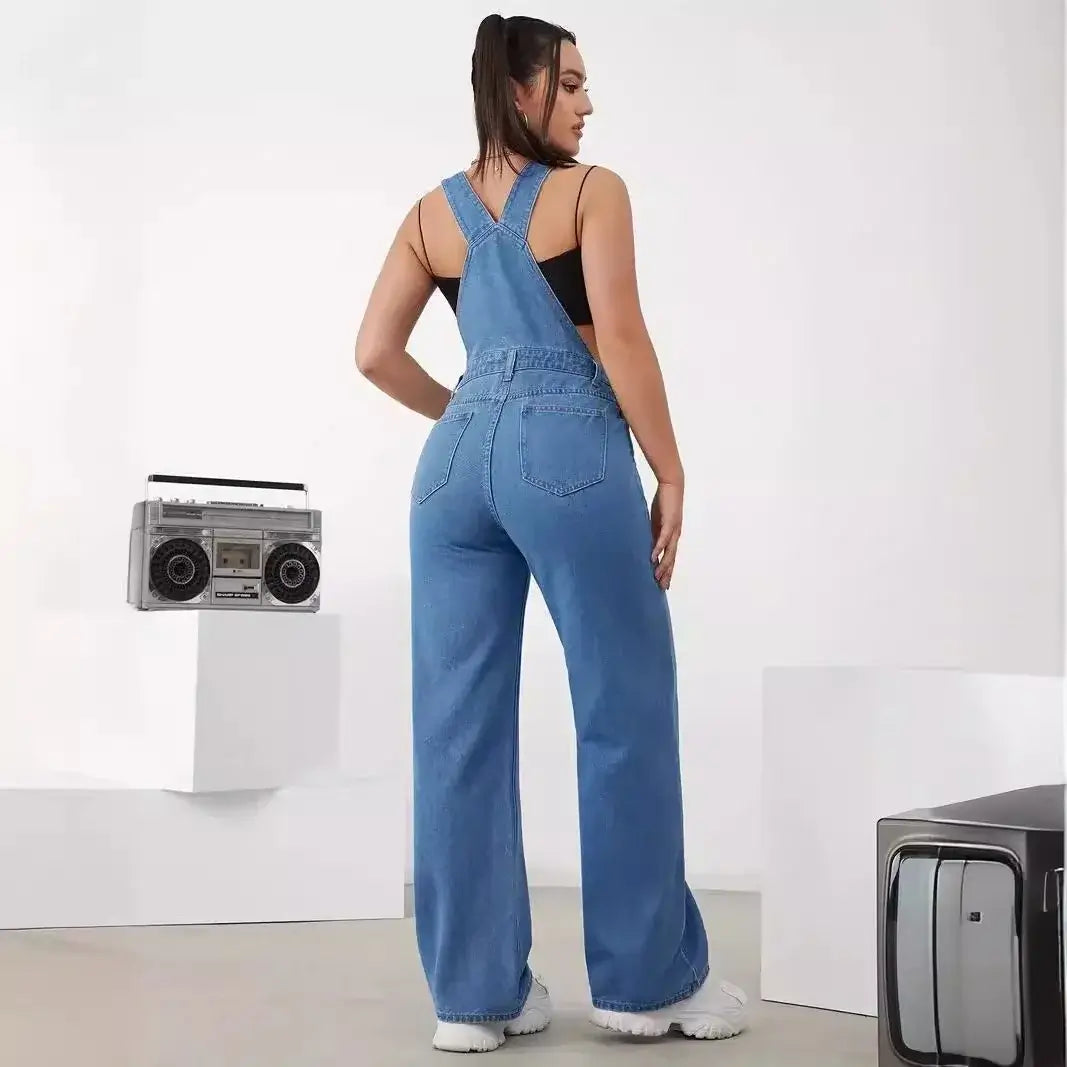 Back view of a woman in a stylish women's denim bib jumpsuit, showcasing adjustable straps and a relaxed fit.