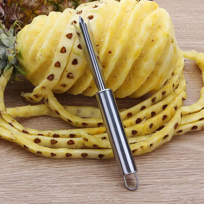 Stainless steel pineapple corer and peeler with swirled pineapple pieces on wooden surface.