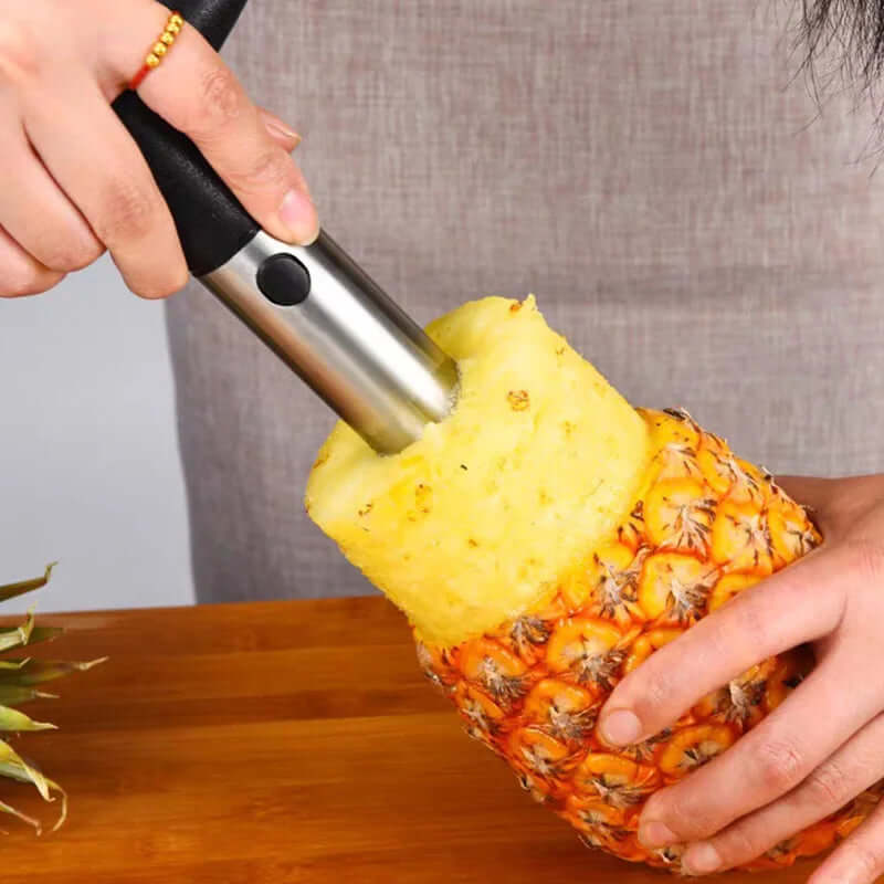 Person using a stainless steel pineapple corer cutter to slice a pineapple, showcasing easy fruit preparation.